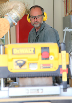 steve maxwell running a board through his DEWALT thickness planer in his home workshop