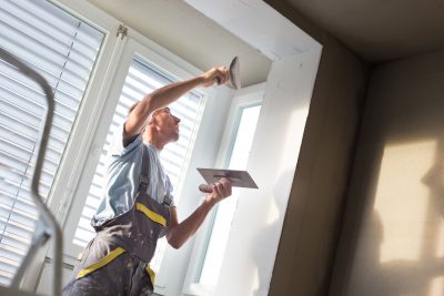 Thirty years old manual worker with wall plastering tools inside a house. Plasterer renovating indoor walls and ceilings with float and plaster.